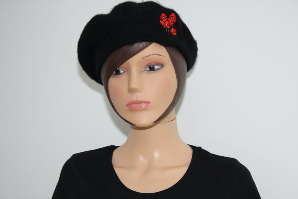 Buste de mannequin avec un béret noir orné de coquelicots rouges et un t-shirt noir.