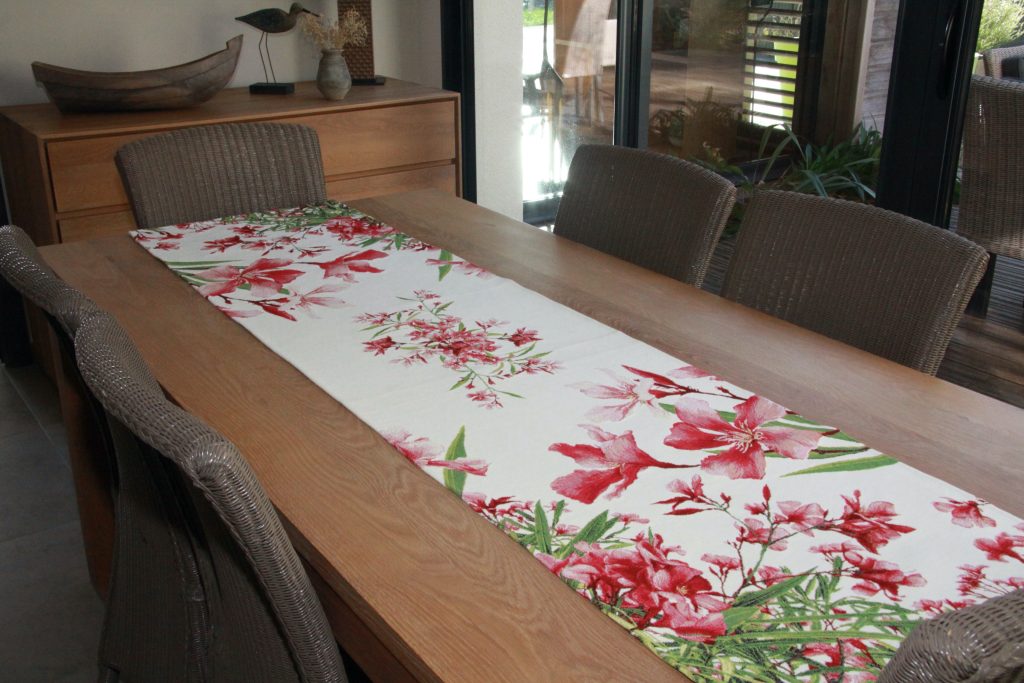 A floral table runner with red patterns, placed on a wooden table.