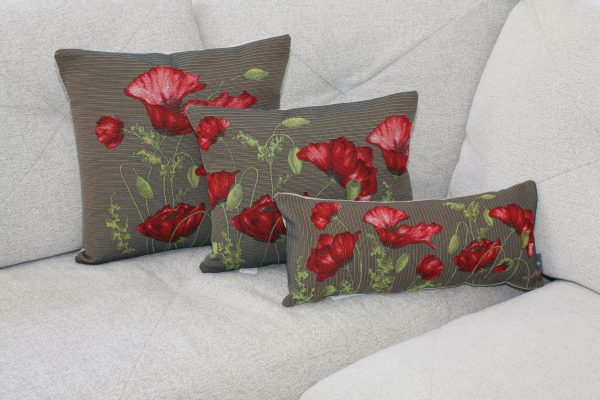 Housse de coussin avec motif de coquelicots rouges sur fond texturé, présentée sur un canapé clair.