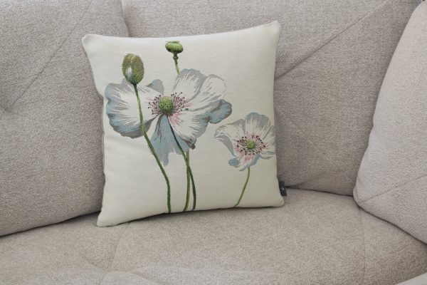 Coussin en tissu jacquard avec motif de coquelicots, assemblé par des artisans français, sur un canapé beige.