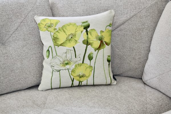 Coussin décoratif avec des motifs de coquelicots jaunes et blancs sur un fond clair, posé sur un canapé gris.