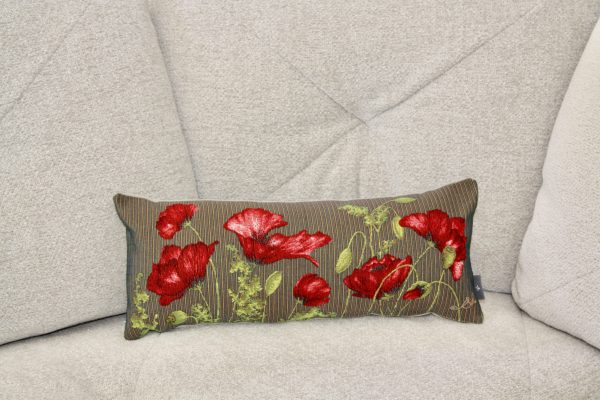Coussin rectangulaire en jacquard avec motifs de coquelicots rouges sur fond rayé, placé sur un canapé gris.
