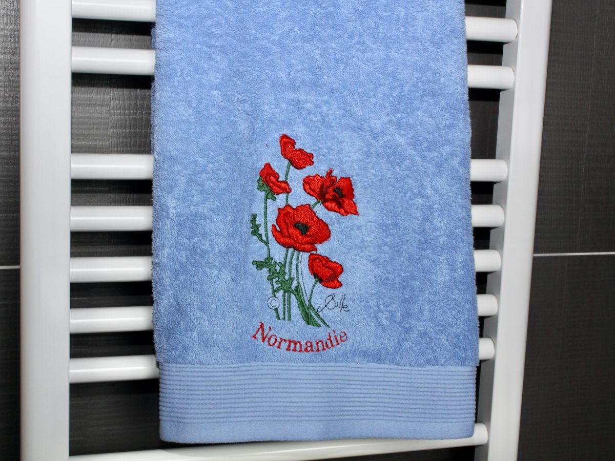 Serviette de toilette bleue avec broderie de coquelicots et inscription "Normandie".