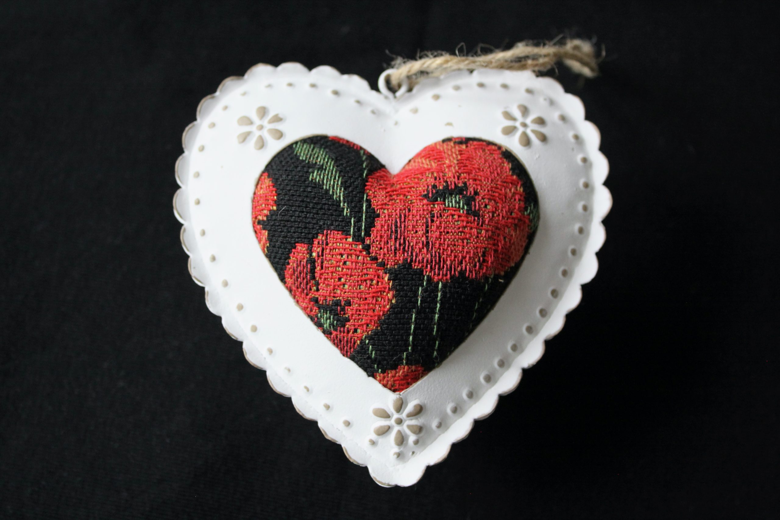 Cœur en métal orné d'un tissu jacquard à motifs de coquelicots, fond noir, présenté dans un support en forme de cœur.