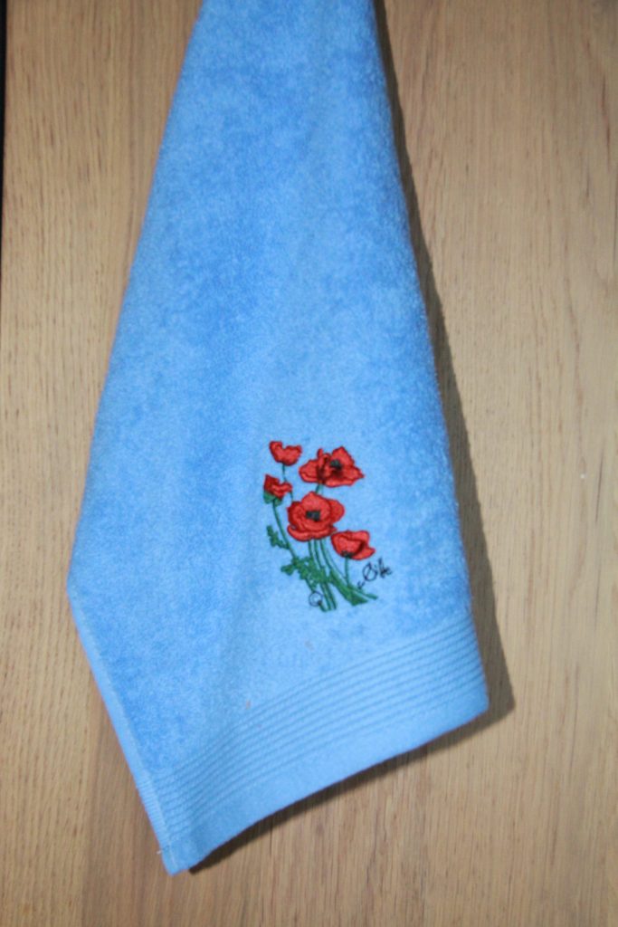 Blue guest towel with poppy embroidery, made in France, reflecting the floral style of Poppies Shop in Bayeux.