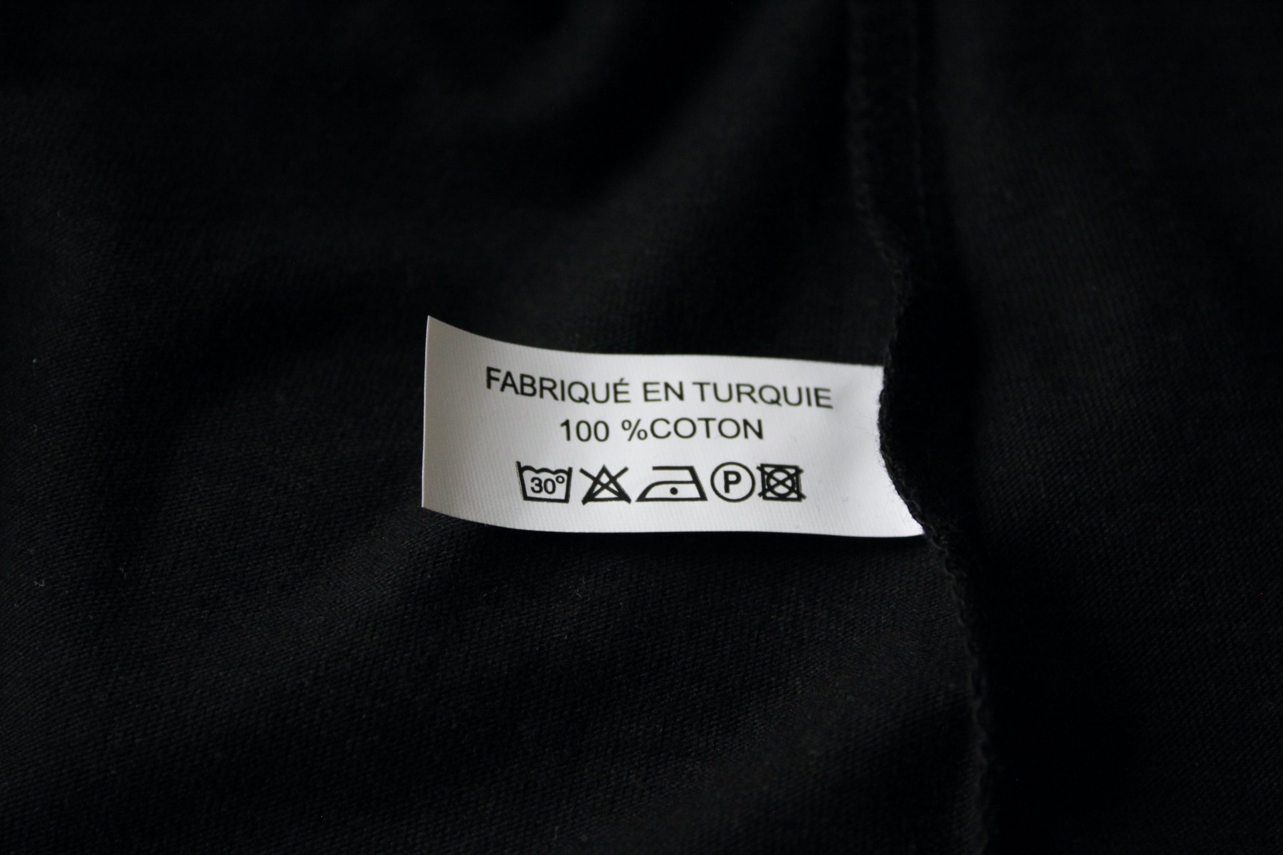 Étiquette d'entretien d'un t-shirt noir en 100% coton, fabriqué en Turquie. Instructions de lavage et de séchage incluses.